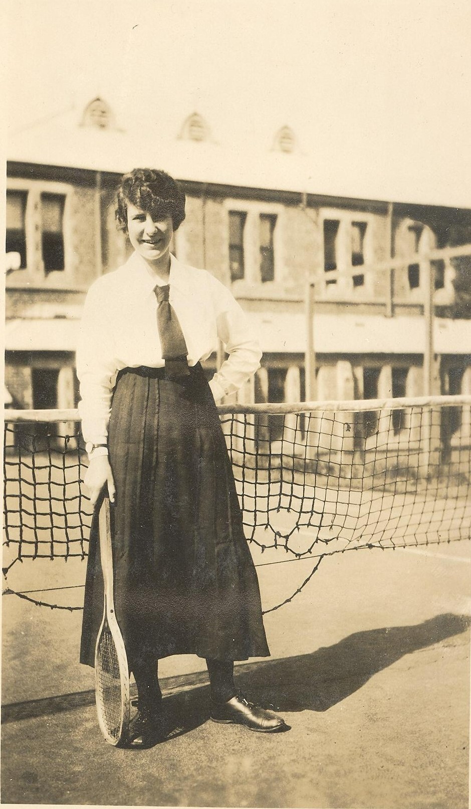 Photo of Winnie Woodmason on MLC tennis court net, with racket, c.1917