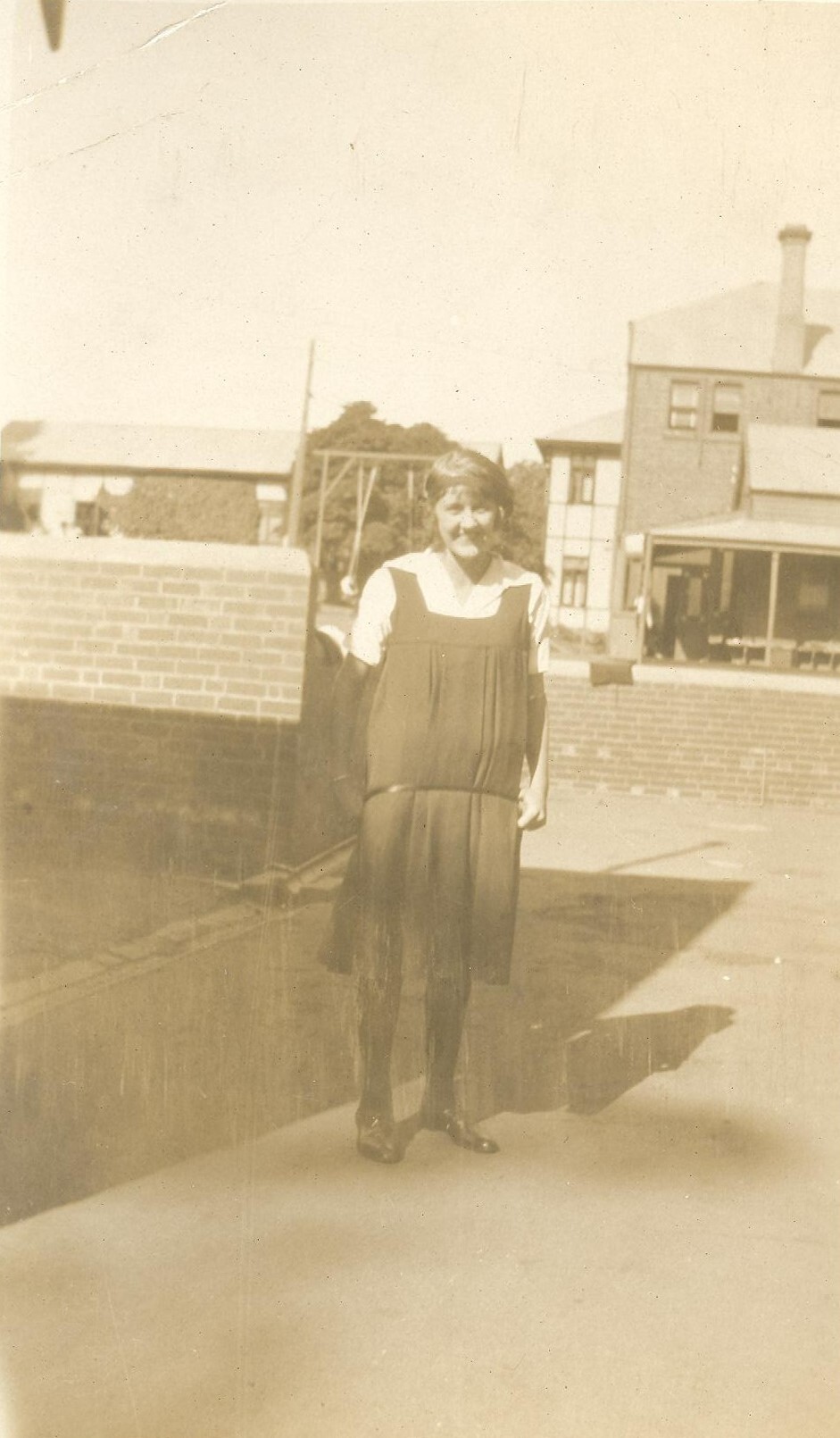 Photo of student standing in school grounds - likely 'quad' area - c.1923