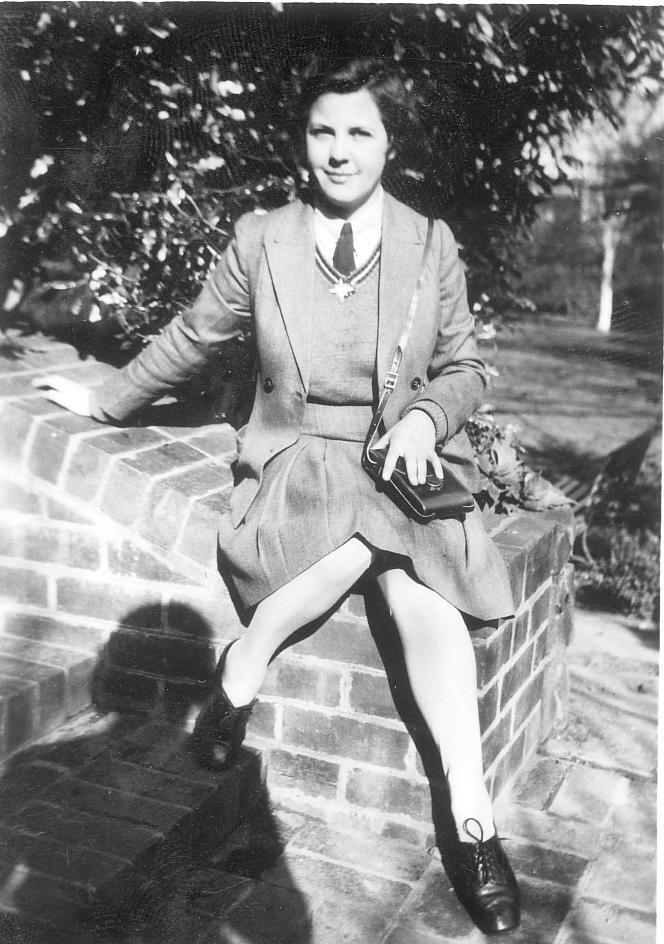 Photograph of Mary Richards in winter uniform seated on brick stairs in front gardens, c.1941