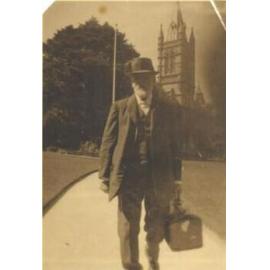 Rev. Dr. Fitchett walking along path from Residence towards Barker's Rd with bag, c.1924