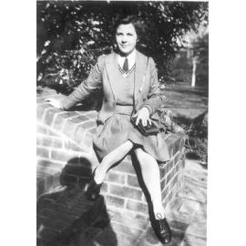Photograph of Mary Richards in winter uniform seated on brick stairs in front gardens, c.1941