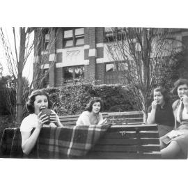 Photo of Betty Raynor, Peg Amos, [Gwen or Margaret?] Sims seated on bench near Fitchett Hall, c.1941