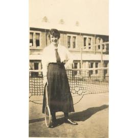 Photo of Winnie Woodmason on MLC tennis court net, with racket, c.1917